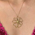 Collier en acier inoxydable doré avec un grand pendentif fleur stylisée aux pétales filaires, porté sur un décolleté.