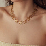Collier en acier inoxydable doré à motifs fleurs ajourées, porté par une femme.