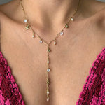 Collier en Y en acier inoxydable doré avec perles, strass et breloques fleurs, porté sur un décolleté.