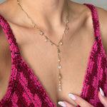 Collier en Y en acier inoxydable doré, avec breloques fleurs, perles et strass clairs, porté sur un décolleté.