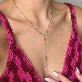 Collier en Y en acier inoxydable doré, avec breloques fleurs, perles et strass clairs, porté sur un décolleté.
