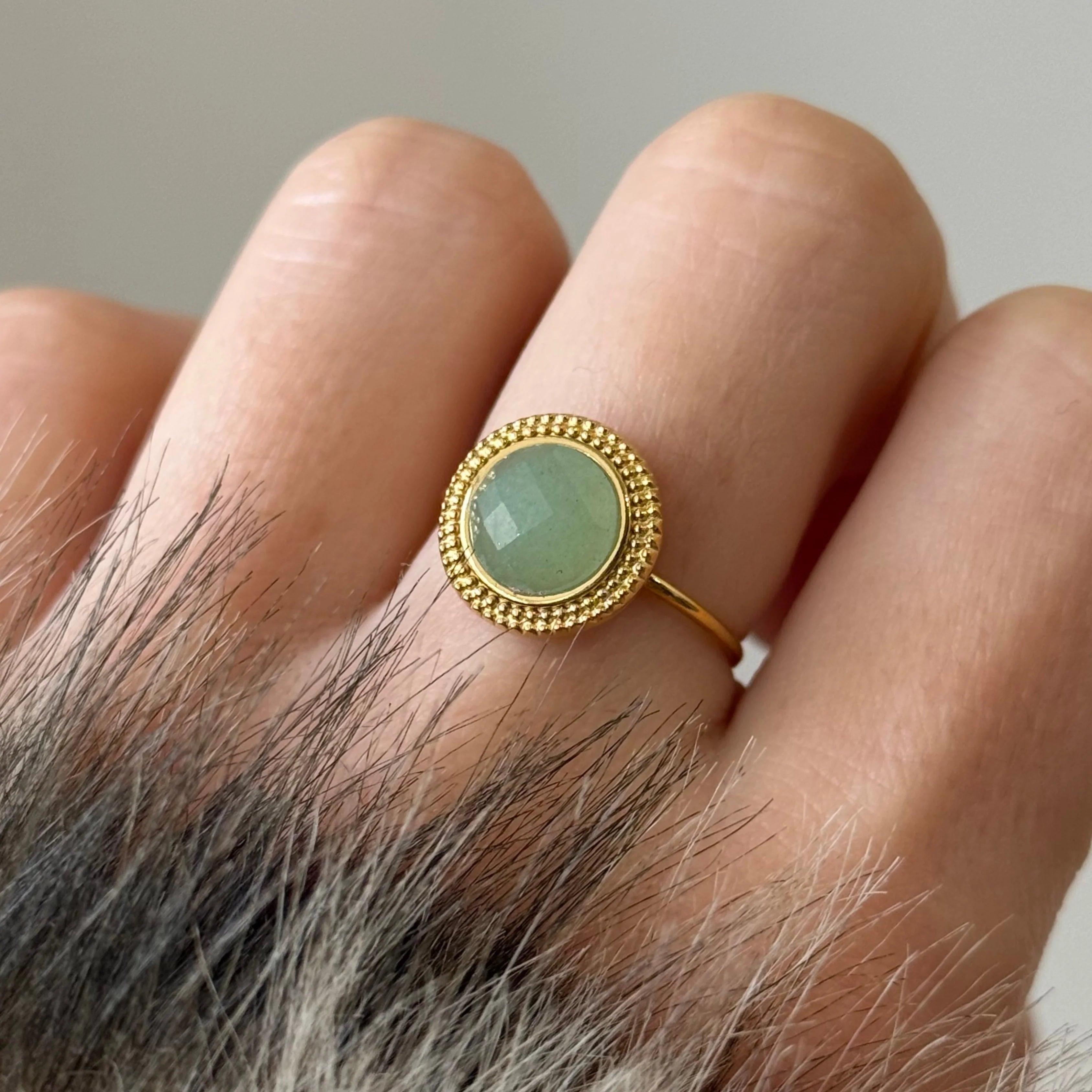 Zoom sur une bague délicate style vintage avec une pierre vert d'eau translucide et une monture perlée dorée.