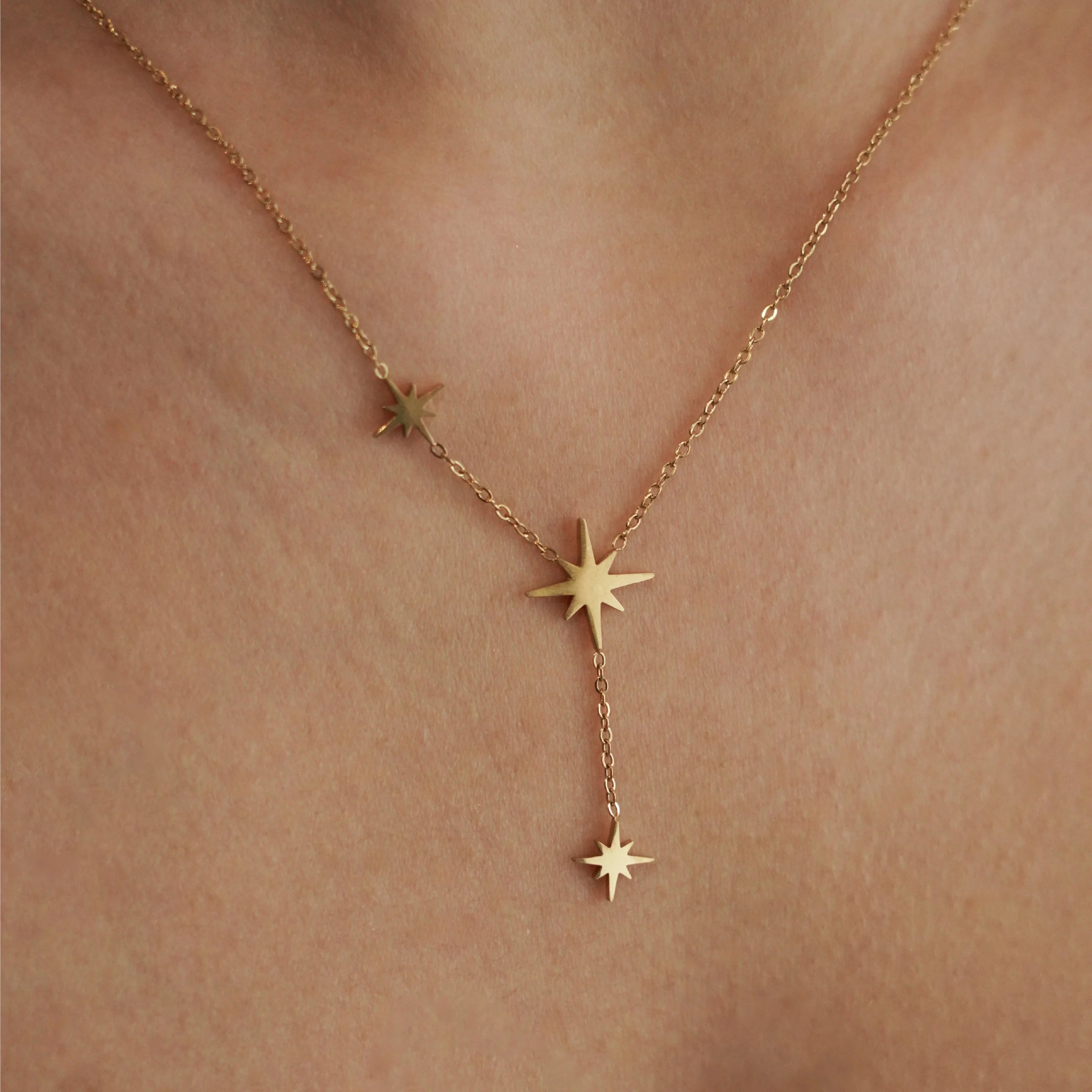 Zoom sur le collier fin doré porté au cou : chaîne délicate et pampilles étoiles polaires, style minimaliste chic.