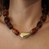 Gros plan sur un collier tendance MAISON DE L'AMOUR porté au cou, perles marron et détail doré chic pour femme.