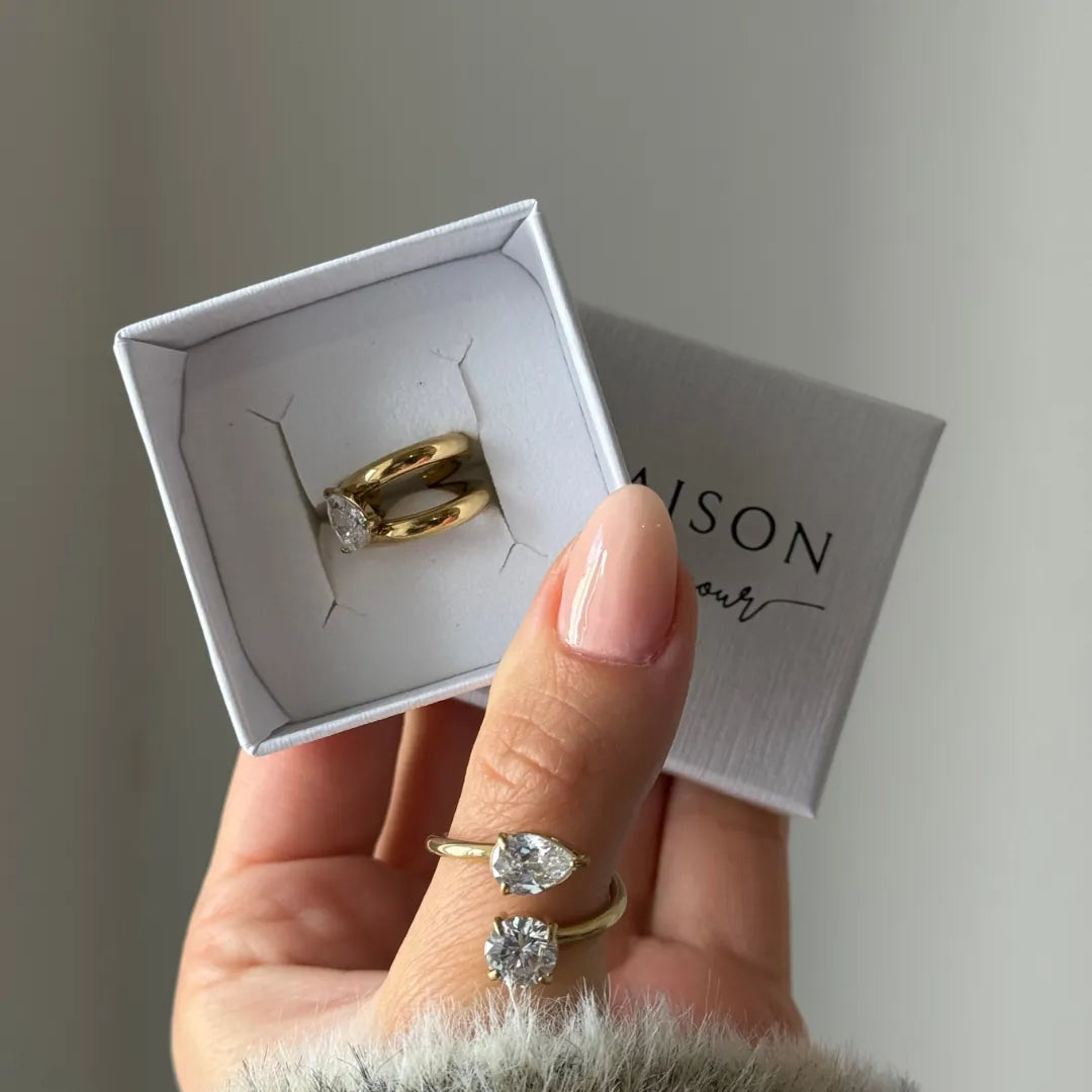 Deux earcuffs en acier inoxydable doré, ornés de zircons. Un earcuff à deux zircons est porté au pouce, un autre à zircon est