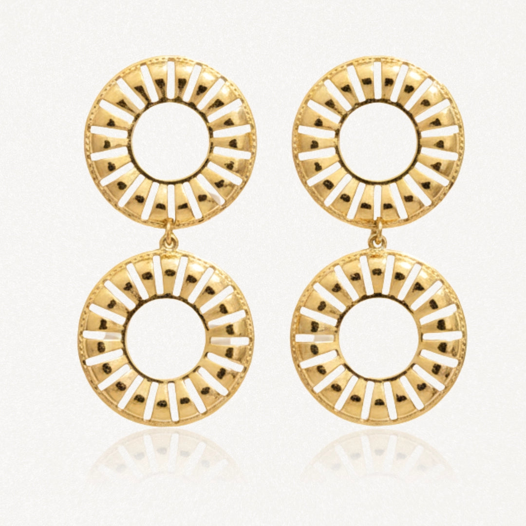 Paire de boucles d'oreilles dorées, pendantes. Chaque boucle a deux anneaux ajourés de motifs radiaux, sur fond blanc.