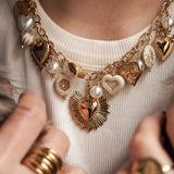 Détail mode : accumulation collier et bracelet cœurs dorés portés avec un manteau en fausse fourrure.