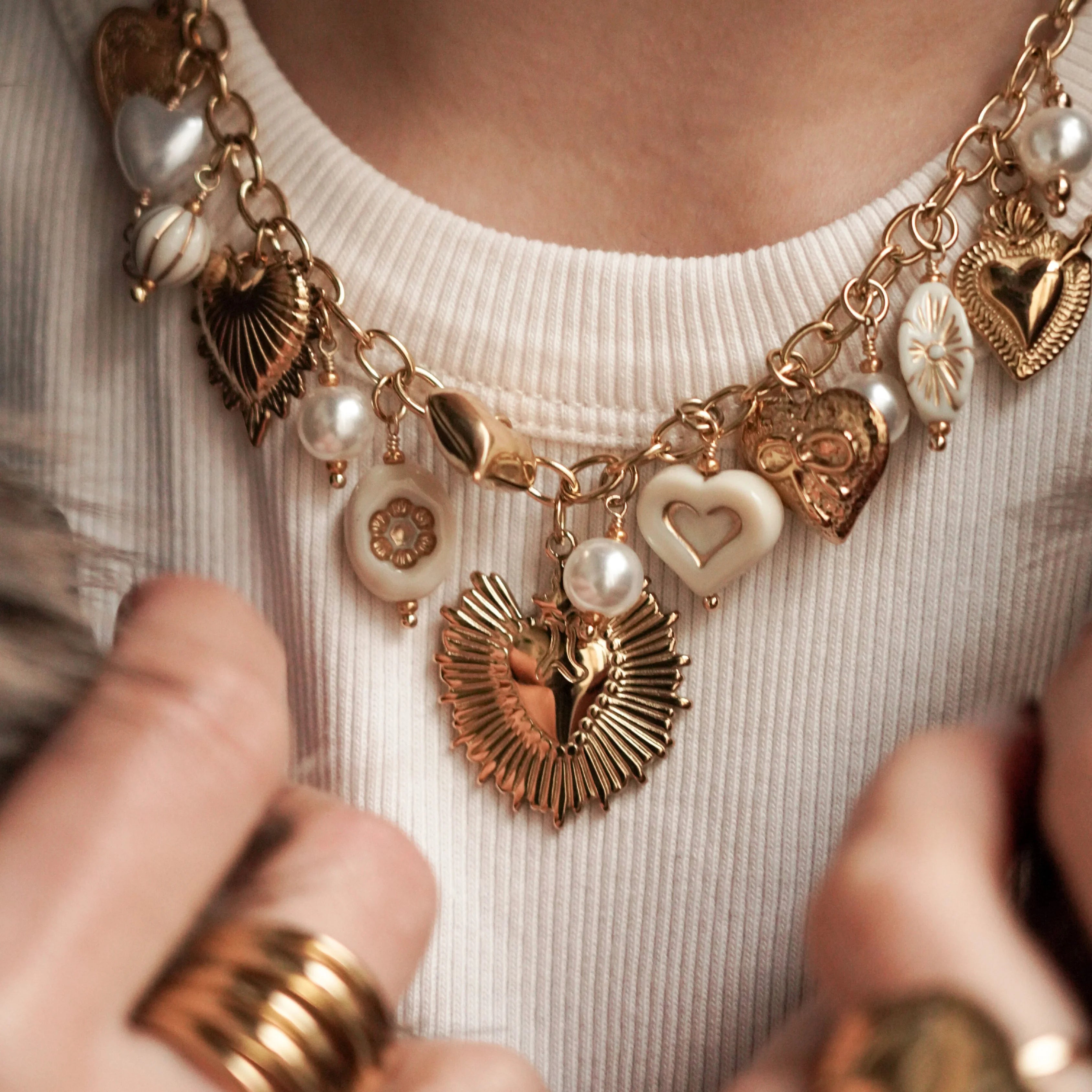 Détail mode : accumulation collier et bracelet cœurs dorés portés avec un manteau en fausse fourrure.