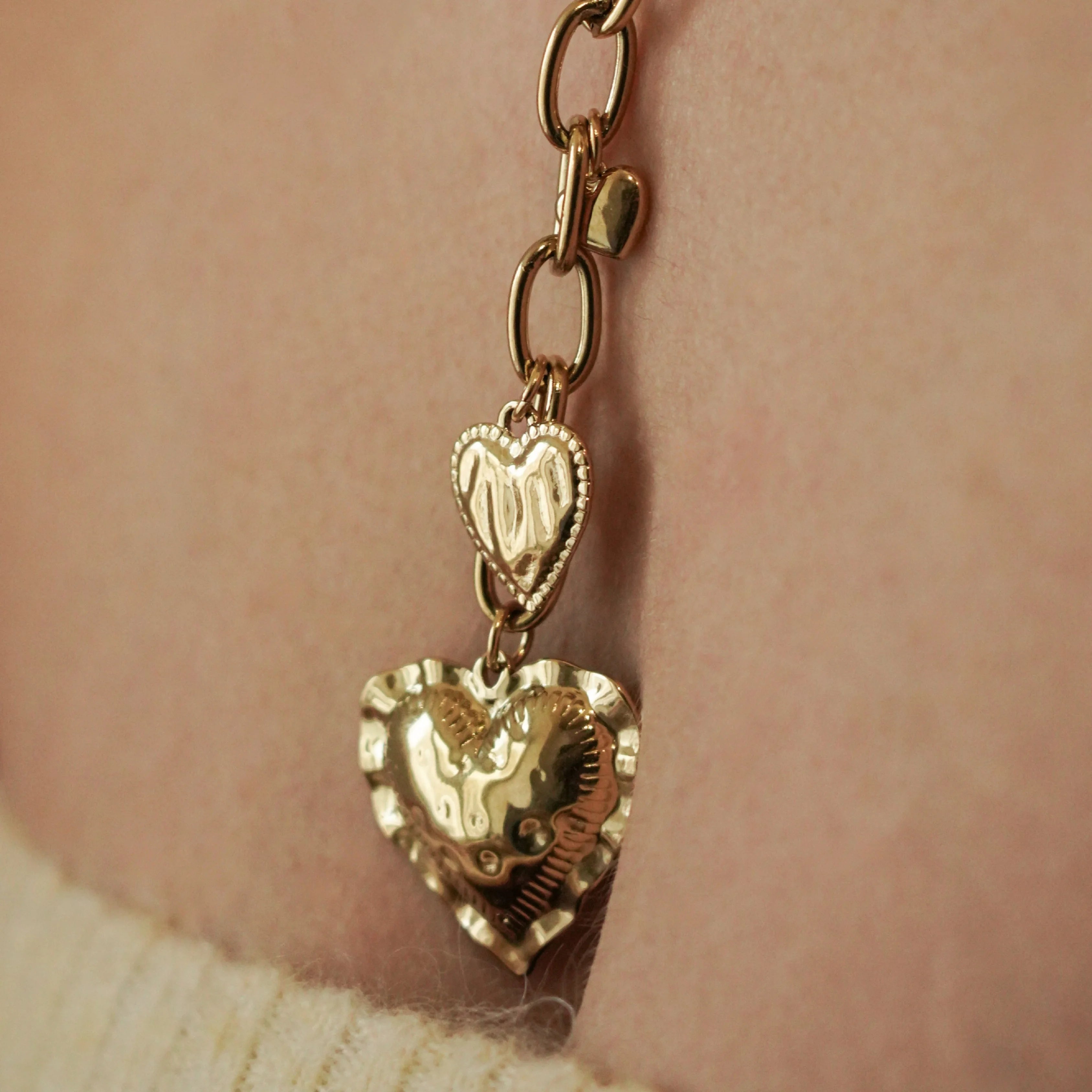 Zoom sur la texture martelée et les finitions soignées des pendentifs cœurs en acier inoxydable doré.