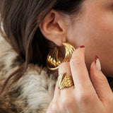 Femme portant des grosses créoles dorées et une bague large assortie, style chic et audacieux.