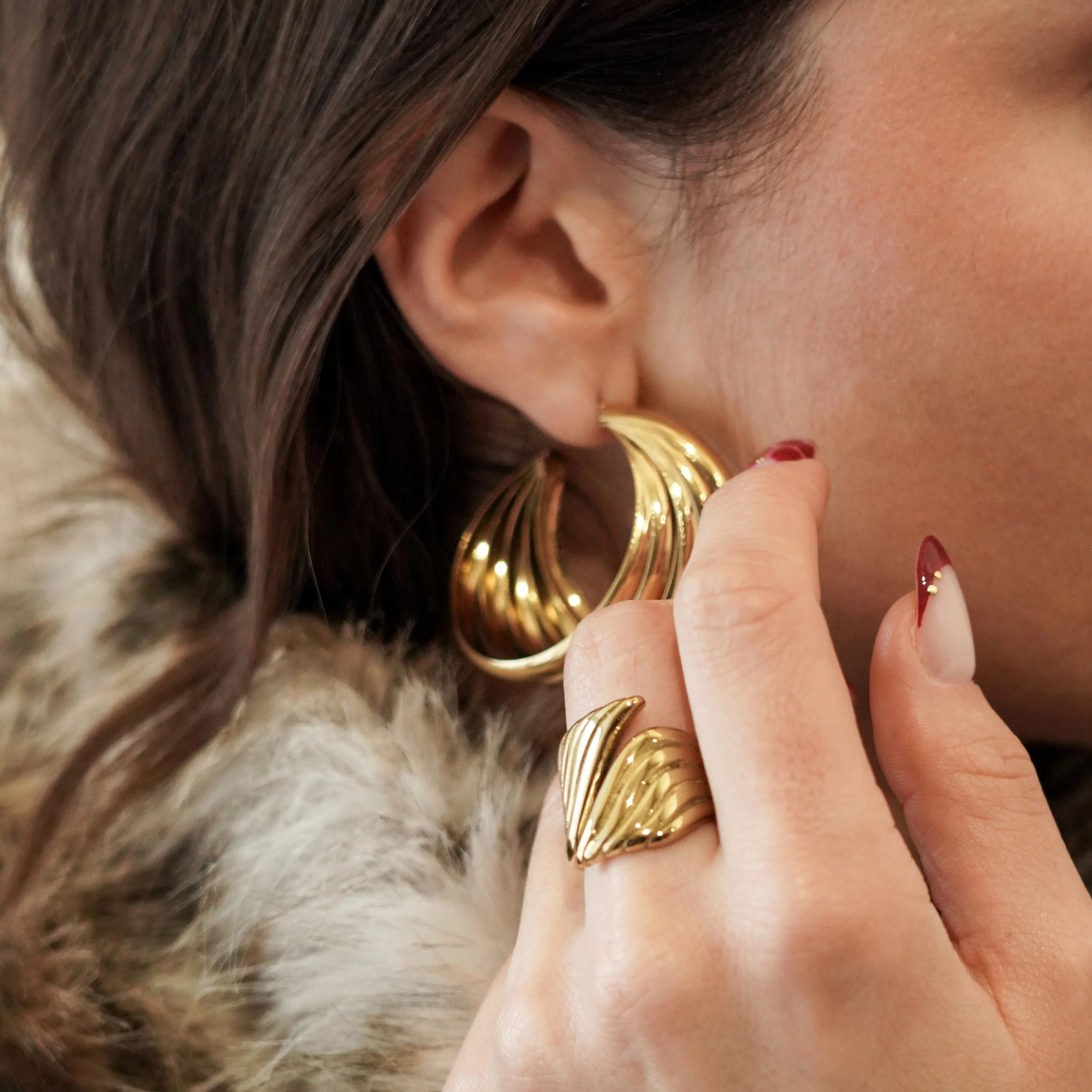 Femme portant des grosses créoles dorées et une bague large assortie, style chic et audacieux.