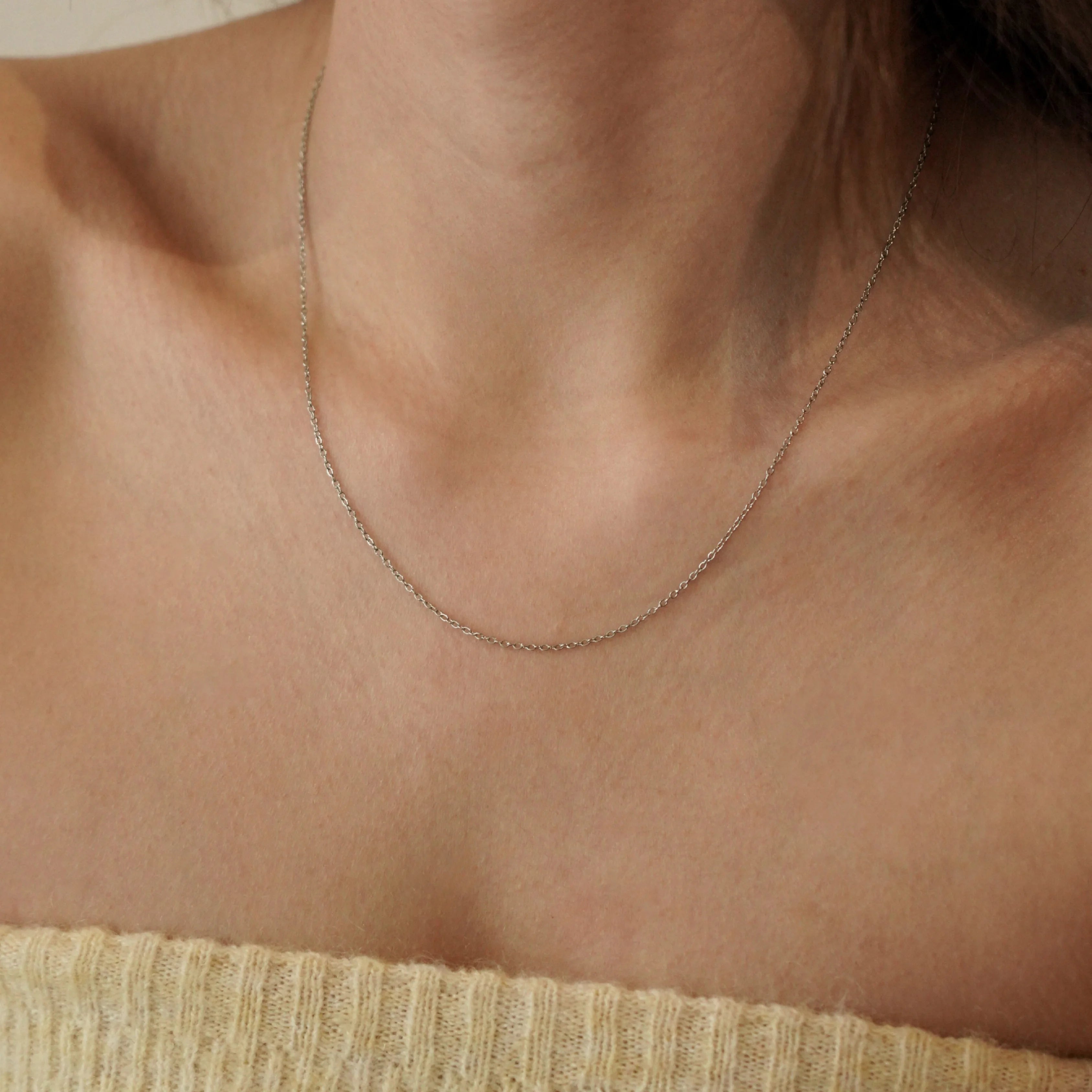 Collier fin argenté porté sur le cou, détail discret et élégant pour une tenue de tous les jours.