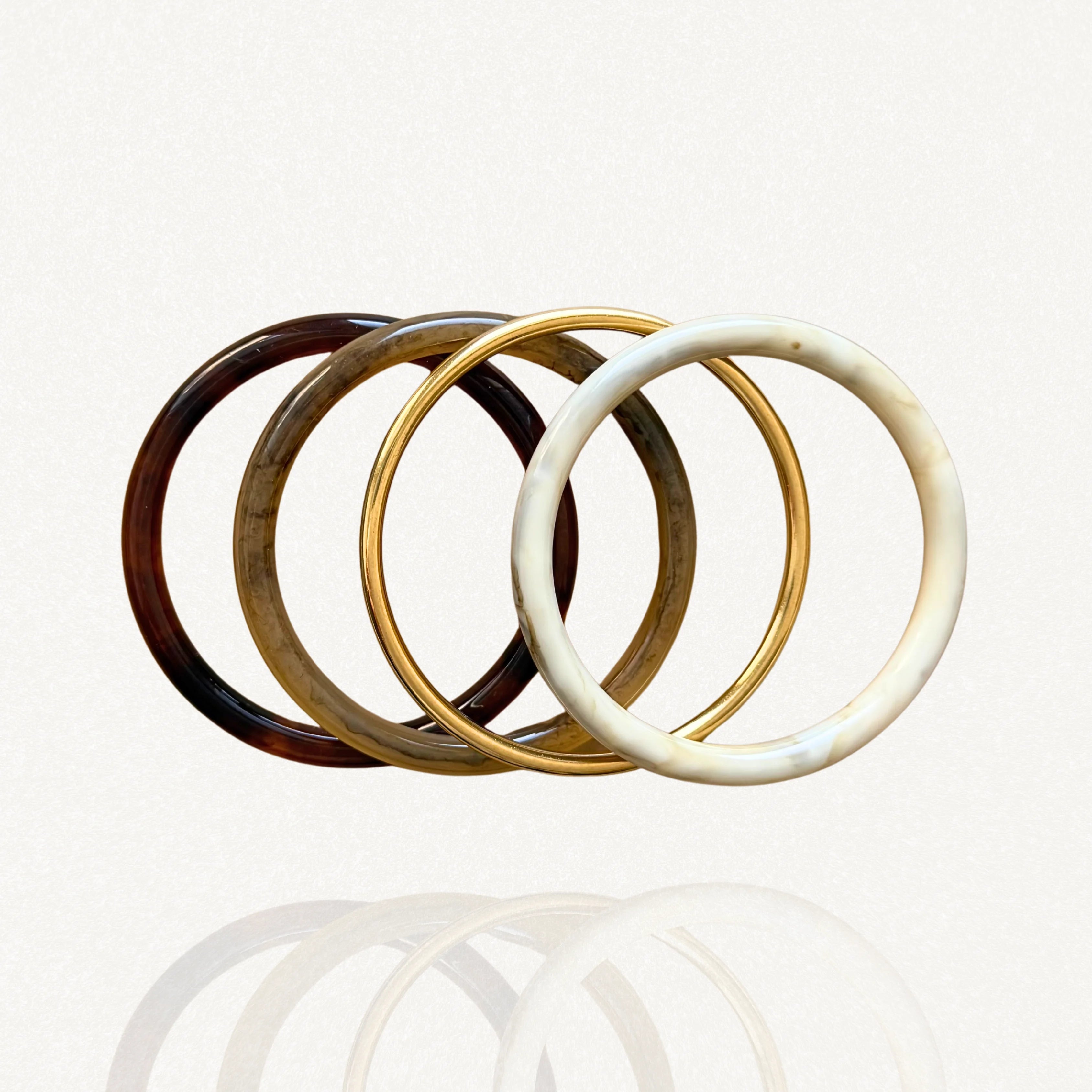 Ensemble de quatre bracelets joncs rigides : résine motif écaille de tortue foncée et claire, effet marbre blanc et métal doré simple sur fond blanc.