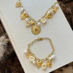 Ensemble collier et bracelet assorti MAISON DE L'AMOUR avec charms cœurs et perles posés sur un livre.