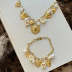 Ensemble de bijoux assortis (parure) composé d'un collier et d'un bracelet chaîne doré avec breloques cœurs et perles, posés sur un livre.