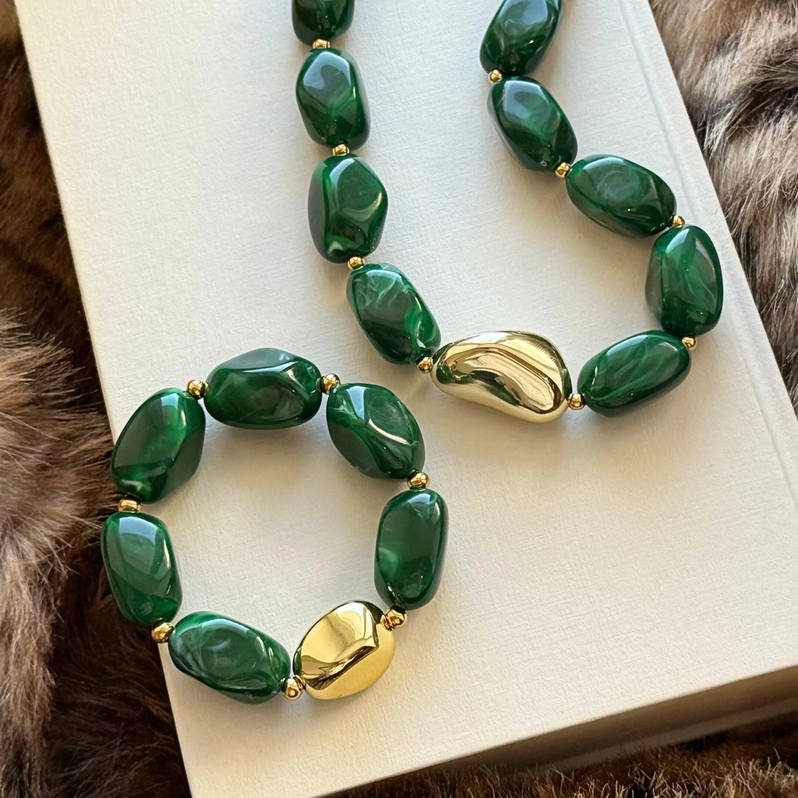 Ensemble parure bijoux tendance posé sur un livre, comprenant un collier et un bracelet assortis avec grosses perles vertes et accent doré.