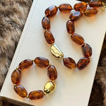 Ensemble collier et bracelet assortis avec grosses perles ovales ambre glacé et fermoir doré posés sur un livre.