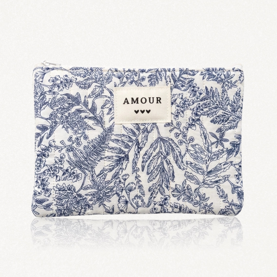 Pochette matelassée à motifs floraux et végétaux bleus sur blanc. Fermeture éclair, et étiquette "AMOUR" avec 3 cœurs.