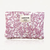 Pochette matelassée blanche à motif floral et feuillage magenta. Étiquette AMOUR avec trois cœurs noirs. Fermeture éclair