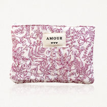 Pochette matelassée blanche à motif floral et feuillage magenta. Étiquette AMOUR avec trois cœurs noirs. Fermeture éclair