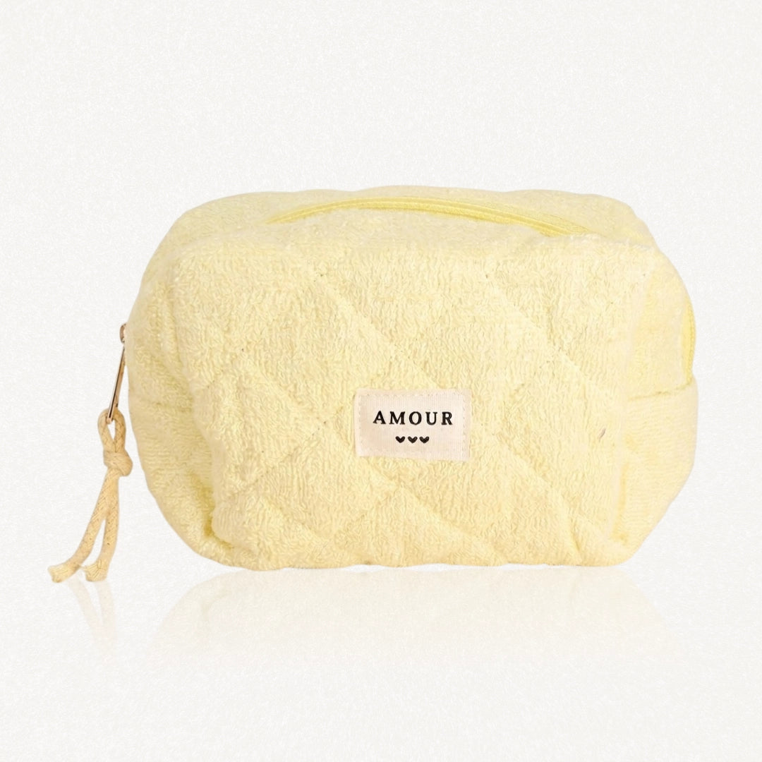 Trousse jaune pâle en tissu éponge matelassé. Fermeture éclair jaune, étiquette "AMOUR" et trois cœurs, cordon tressé.