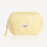 Trousse jaune pâle en tissu éponge matelassé. Fermeture éclair jaune, étiquette "AMOUR" et trois cœurs, cordon tressé.