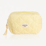 Trousse jaune pâle en tissu éponge matelassé. Fermeture éclair jaune, étiquette "AMOUR" et trois cœurs, cordon tressé.