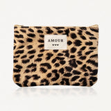 Pochette à imprimé léopard, rectangulaire, avec fermeture éclair beige. Étiquette blanche "AMOUR" et trois cœurs noirs.