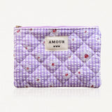 Pochette matelassée à carreaux vichy violets et blancs, fleurs de marguerites. Fermeture éclair lilas. Étiquette "AMOUR" et 3