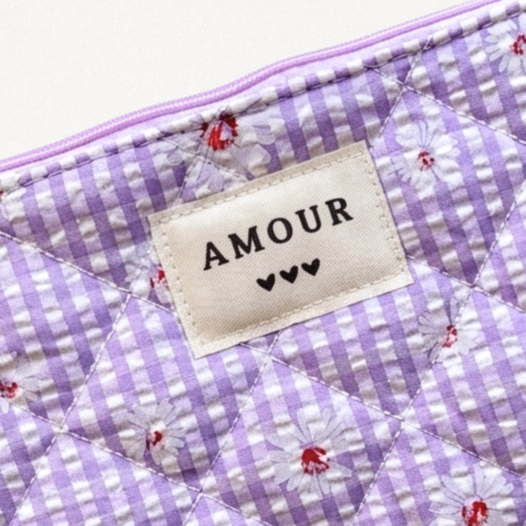 Pochette matelassée lilas à carreaux vichy avec marguerites blanches. Étiquette "AMOUR" et 3 cœurs noirs.