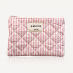 Pochette matelassée à rayures roses et blanches. Fermeture éclair rose. Étiquette crème "AMOUR" et 3 cœurs noirs.