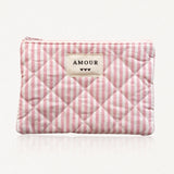 Pochette matelassée à rayures roses et blanches. Fermeture éclair rose. Étiquette crème "AMOUR" et 3 cœurs noirs.