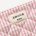 Pochette matelassée rose et blanche à rayures. Étiquette en tissu crème brodée "AMOUR" et 3 cœurs noirs.