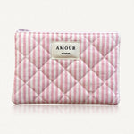 Pochette matelassée à rayures roses et blanches. Fermeture éclair rose. Étiquette crème "AMOUR" et 3 cœurs noirs.
