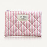 Pochette matelassée à rayures roses et blanches. Fermeture éclair rose. Étiquette crème "AMOUR" et 3 cœurs noirs.