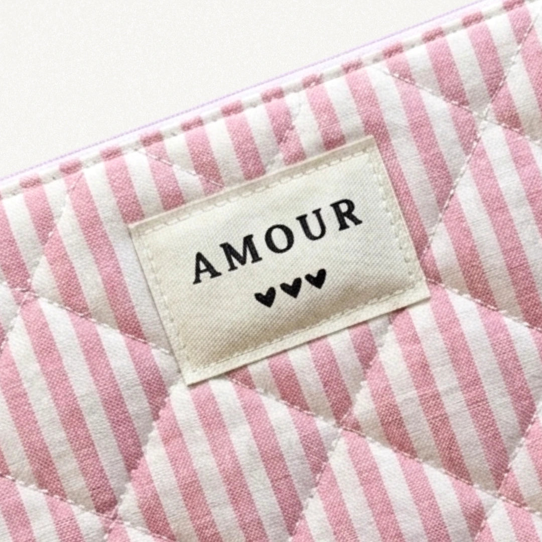 Pochette matelassée rose et blanche à rayures. Étiquette en tissu crème brodée "AMOUR" et 3 cœurs noirs.