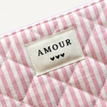Pochette matelassée rose et blanche à rayures. Étiquette en tissu crème brodée "AMOUR" et 3 cœurs noirs.