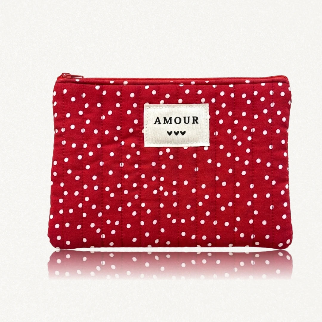 Pochette rouge matelassée de losanges, à pois blancs. Étiquette beige "AMOUR" avec trois cœurs noirs, et fermeture éclair