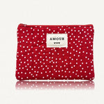 Pochette rouge matelassée de losanges, à pois blancs. Étiquette beige "AMOUR" avec trois cœurs noirs, et fermeture éclair