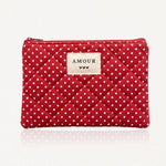 Pochette rouge matelassée de losanges, à pois blancs. Étiquette beige "AMOUR" avec trois cœurs noirs, et fermeture éclair