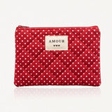 Pochette rouge matelassée de losanges, à pois blancs. Étiquette beige "AMOUR" avec trois cœurs noirs, et fermeture éclair