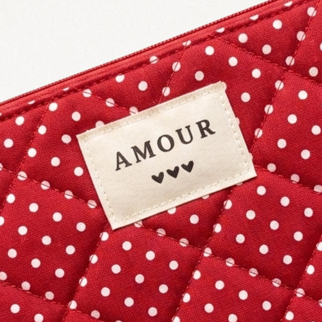 Pochette matelassée rouge à pois blancs. Étiquette beige brodée AMOUR et trois petits cœurs noirs. Fermeture éclair rouge en