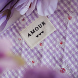 Fond pour bague en acier inoxydable: tissu vichy violet à marguerites, étiquette Amour avec cœurs, et fleurs floues.