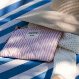 Pochette matelassée rose à rayures blanches avec l'inscription AMOUR, posée sur une serviette bleue près d'un chapeau de