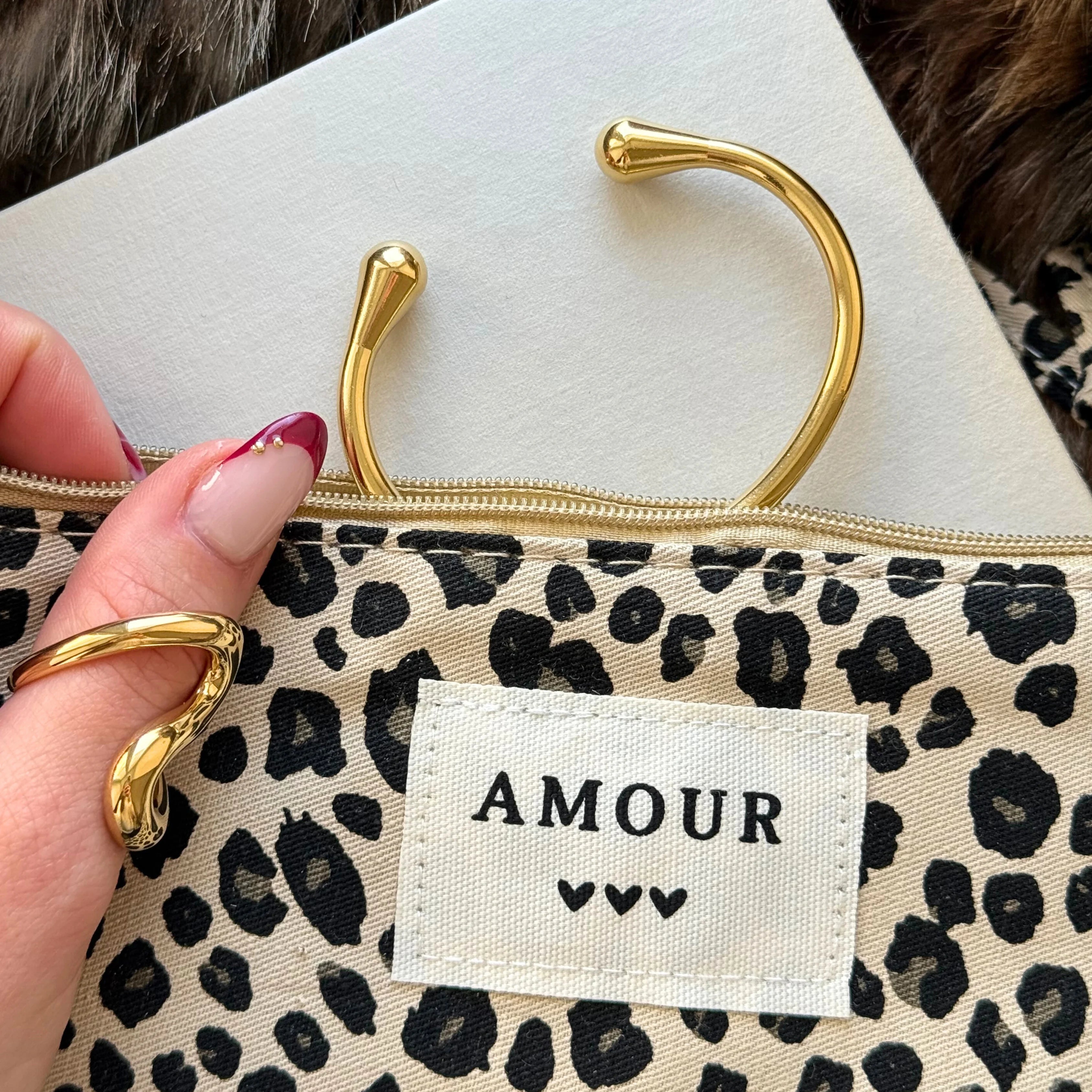 Bague et bracelet jonc ouverts dorés disposés dans une trousse à motif léopard avec étiquette brodée Amour.
