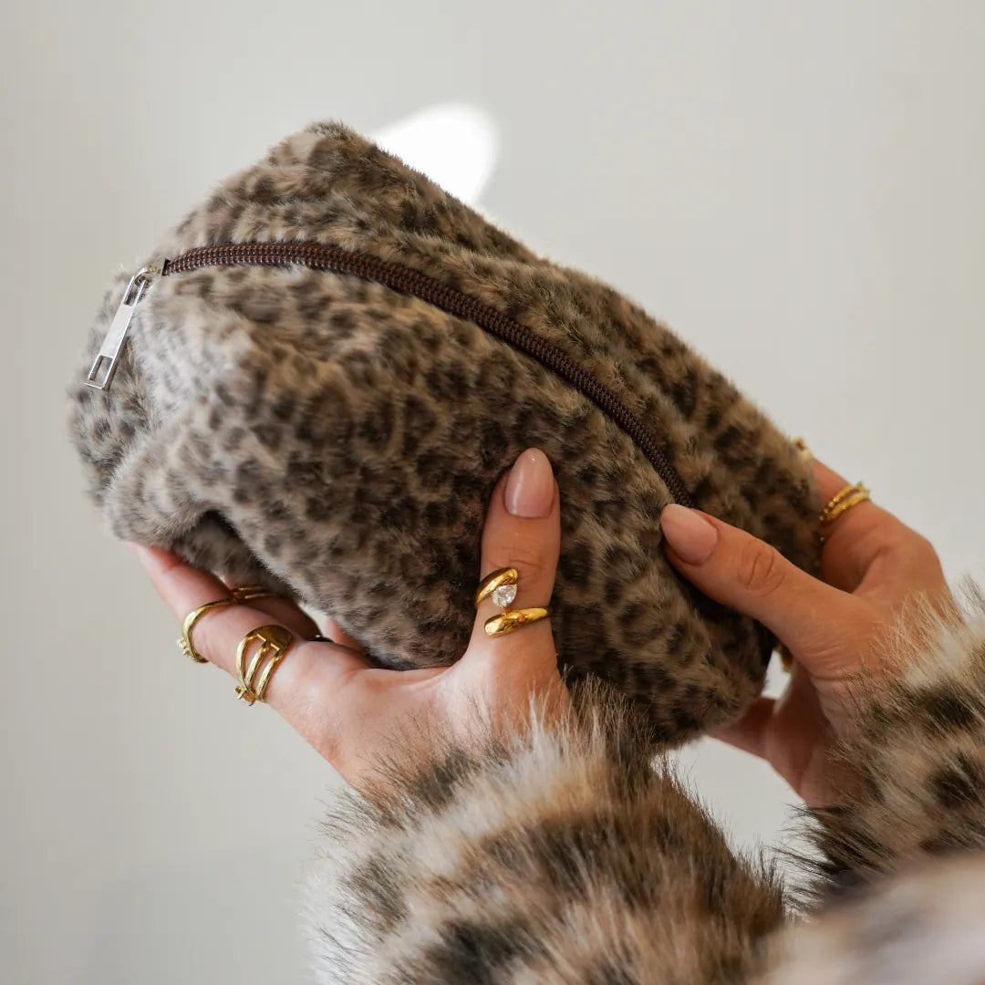 Deux mains tiennent une pochette en polyester doux motif léopard sable (beige et marron) avec fermeture éclair et curseur