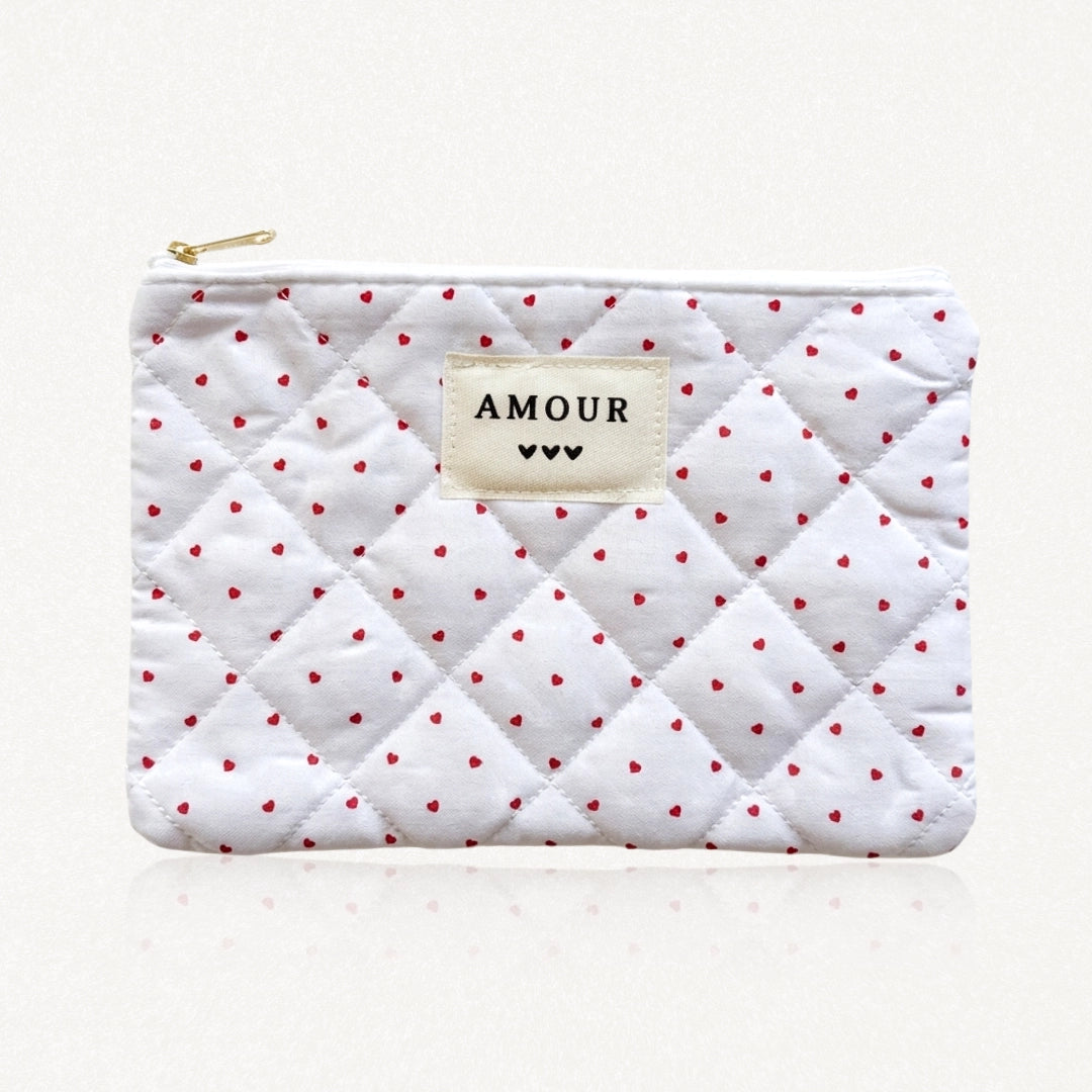 Pochette matelassée blanche à motifs petits cœurs rouges. Étiquette "AMOUR" et 3 cœurs noirs cousue au centre. Fermeture