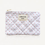 Pochette matelassée blanche à motifs petits cœurs rouges. Étiquette "AMOUR" et 3 cœurs noirs cousue au centre. Fermeture
