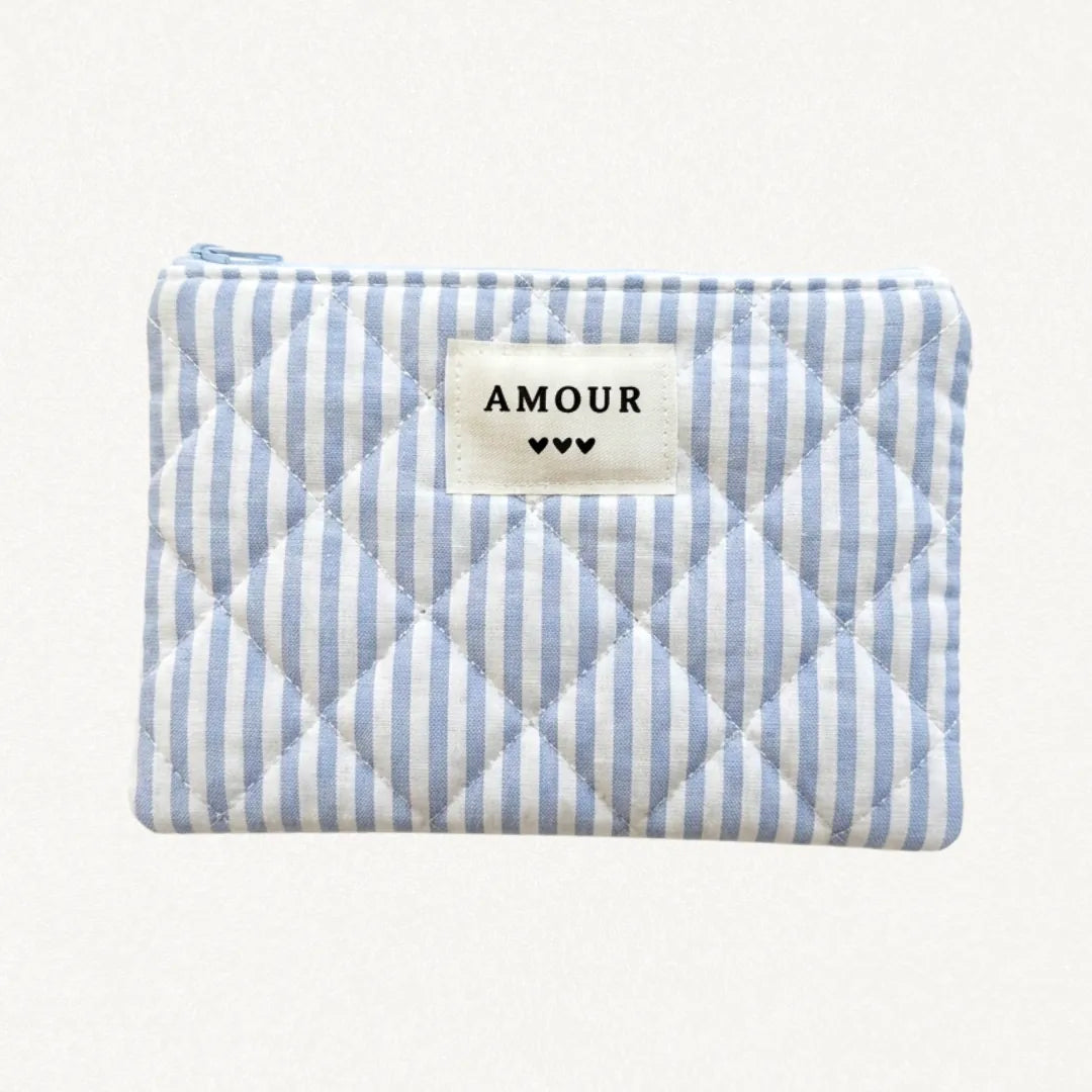 Pochette matelassée à rayures verticales bleues et blanches, avec étiquette "AMOUR" et 3 coeurs noirs. Fermeture éclair