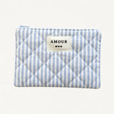 Pochette matelassée à rayures verticales bleues et blanches, avec étiquette "AMOUR" et 3 coeurs noirs. Fermeture éclair